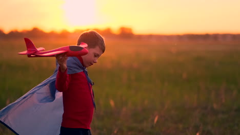 Boy-pilot-runs-in-a-red-raincoat-holding-a-plane-laughing-at-sunset-in-the-summer-field-imagining-that-he-is-an-airplane-pilot-playing-with-a-model-airplane